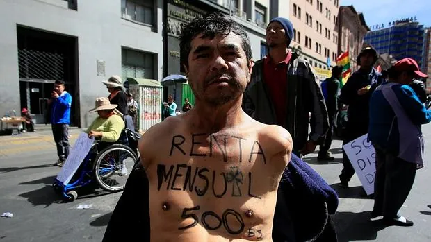 Un manifestante con una discapacidad física muestra el lema de "subsidio mensual de quinientos bolivianos"