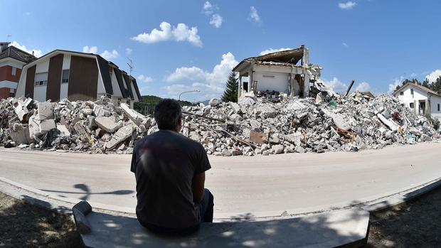 Un hombre se sienta enfrente de varias casas derrumbadas por el terremoto en Amatrice