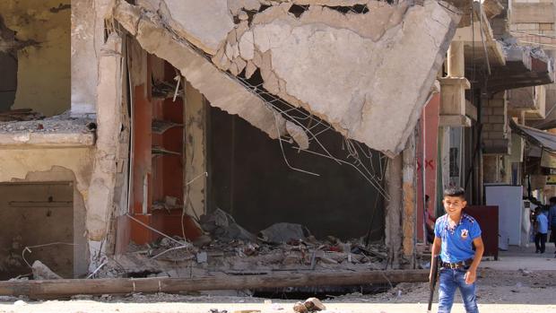 Un niño con una arma de jugete pasa junto a un edificio en ruinas en la ciudad siria de Qamishli el pasado 13 de septiembre, dos días después de que se decretase una tregua