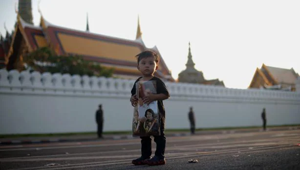 Un niño con la fotografía de la Familia Real junto al Palacio de Bangkok