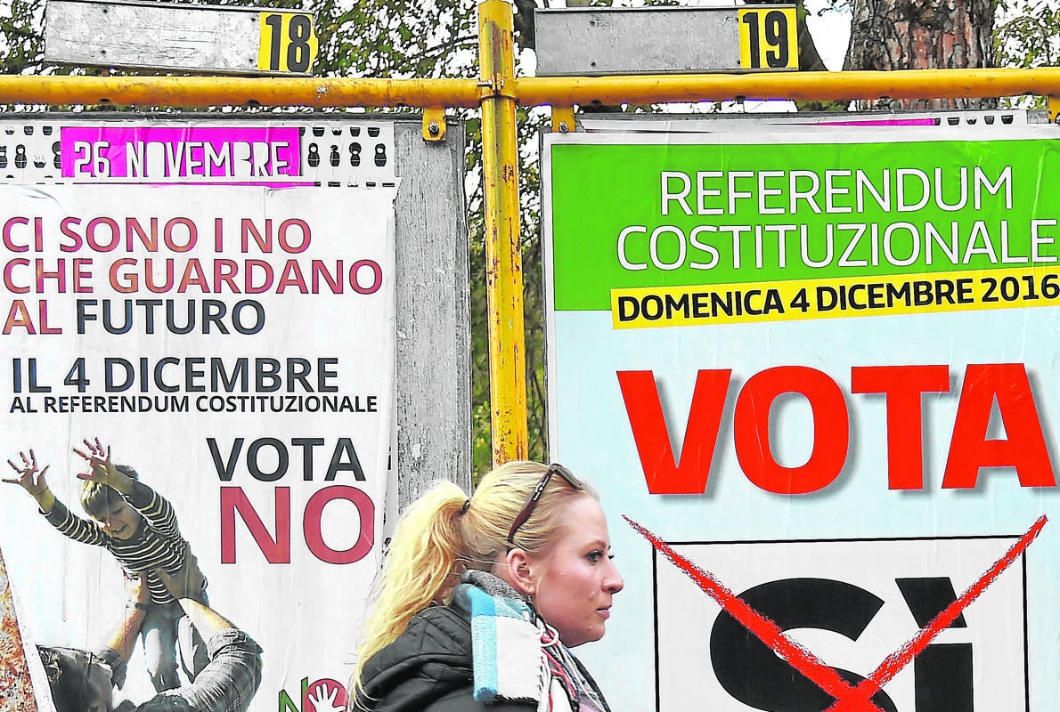 Una mujer camina en Roma junto a propaganda electoral de la consulta