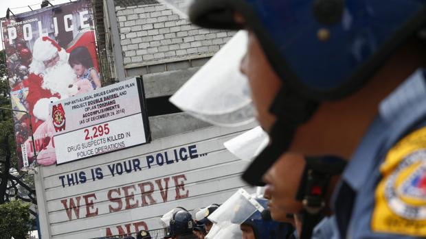 Policías vigilan a manifestantes que protestan contra la brutalidad policiial y los asesinats extrajudiciales en la campaña antidrogas del presidente Rodrigo Duterte, este viernes en Quezón