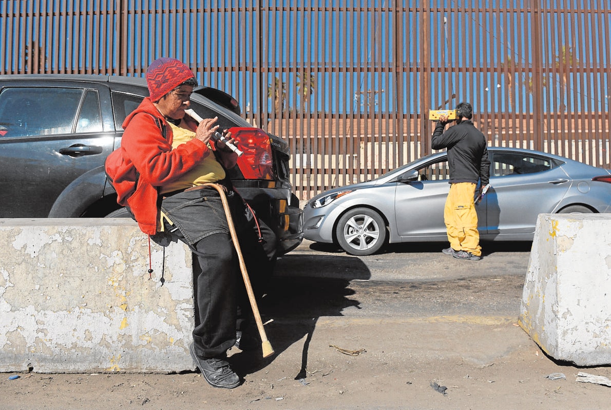 Una mujer pide junto a una valla fronteriza entre México y Estados Unidos