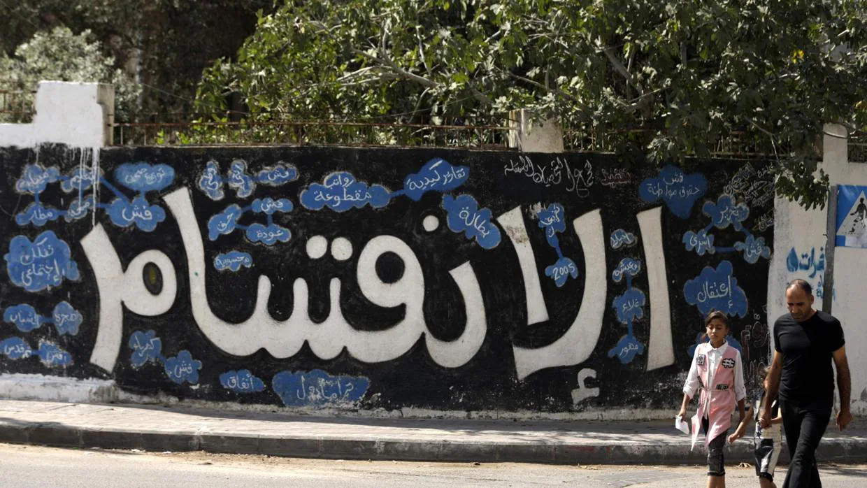 Un palestino y su hija pasan delante de un mural en Gaza en el que se lee «División»