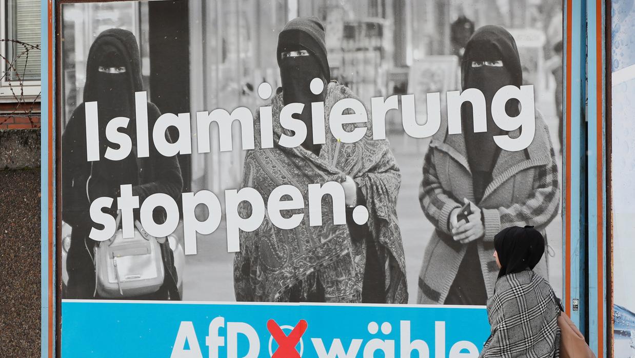 Una mujer con la cabeza cubierta pasa frente a un cartel de AfD