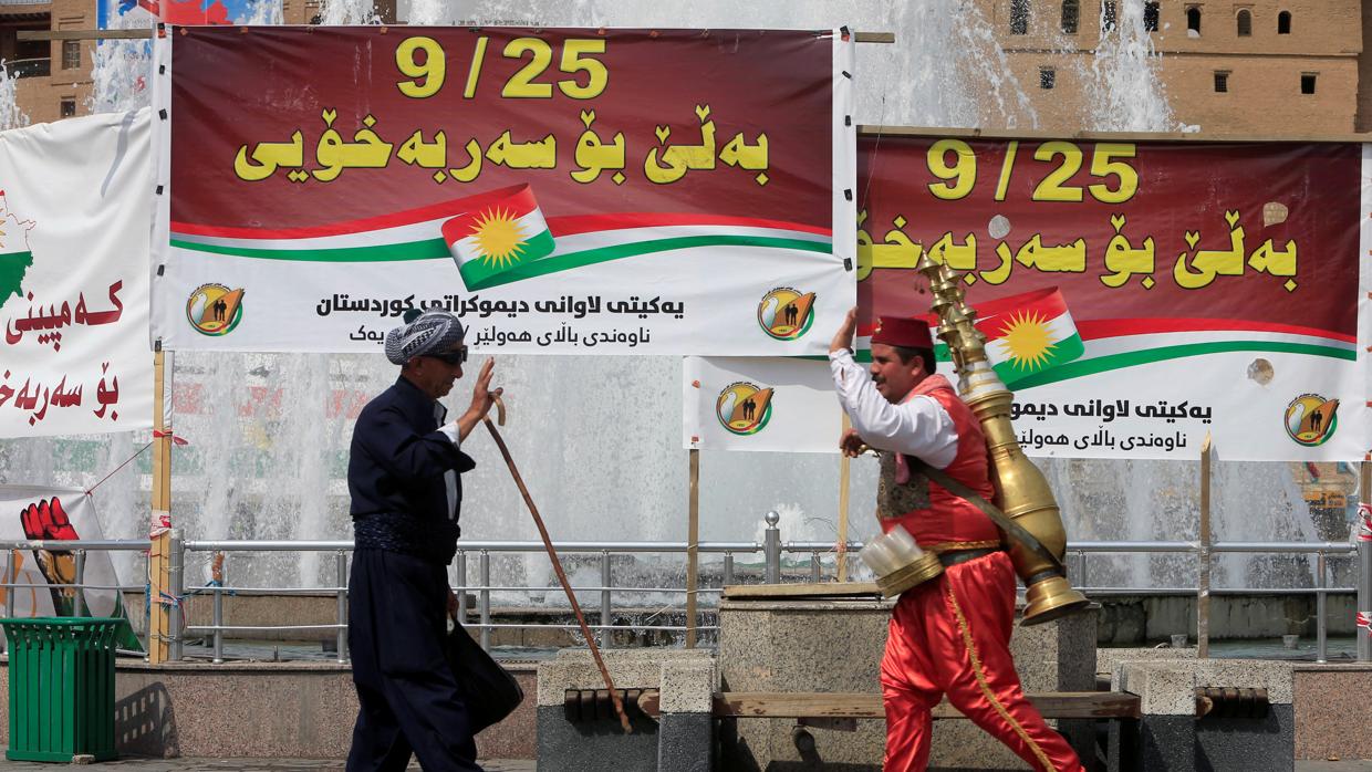 Dos hombres se saludan en un mercado a unos carteles llamando a votar en el referéndum independentista