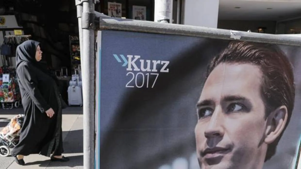 Una mujer camina detrás de un cartel de la campaña de Sebastian Kurz, el favorito