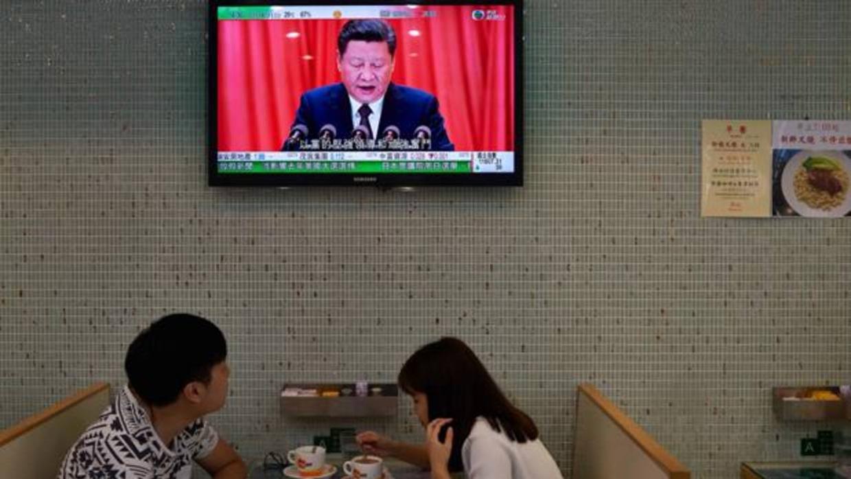 Una pareja almuerza en un café en Hong Kong bajo una televisión que muestra al presidente de China, Xi Jinping