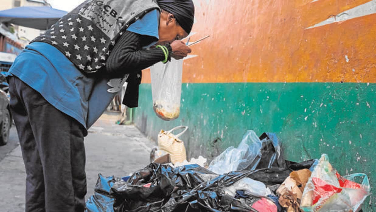 Una mujer hurga en la basura en una calle de Caracas