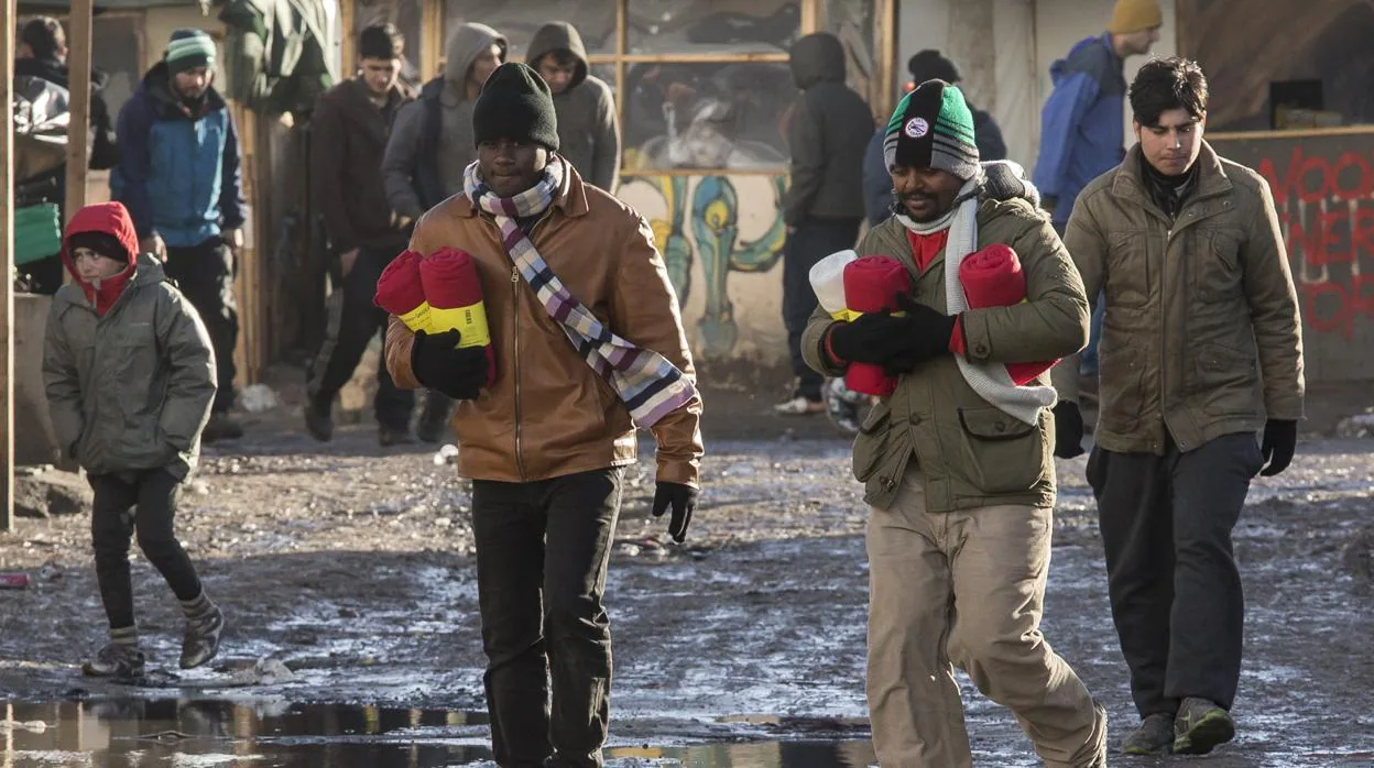 Refugiados se dirigen con mantas hacia sus tiendas de campaña en el campamento «La Jungla»