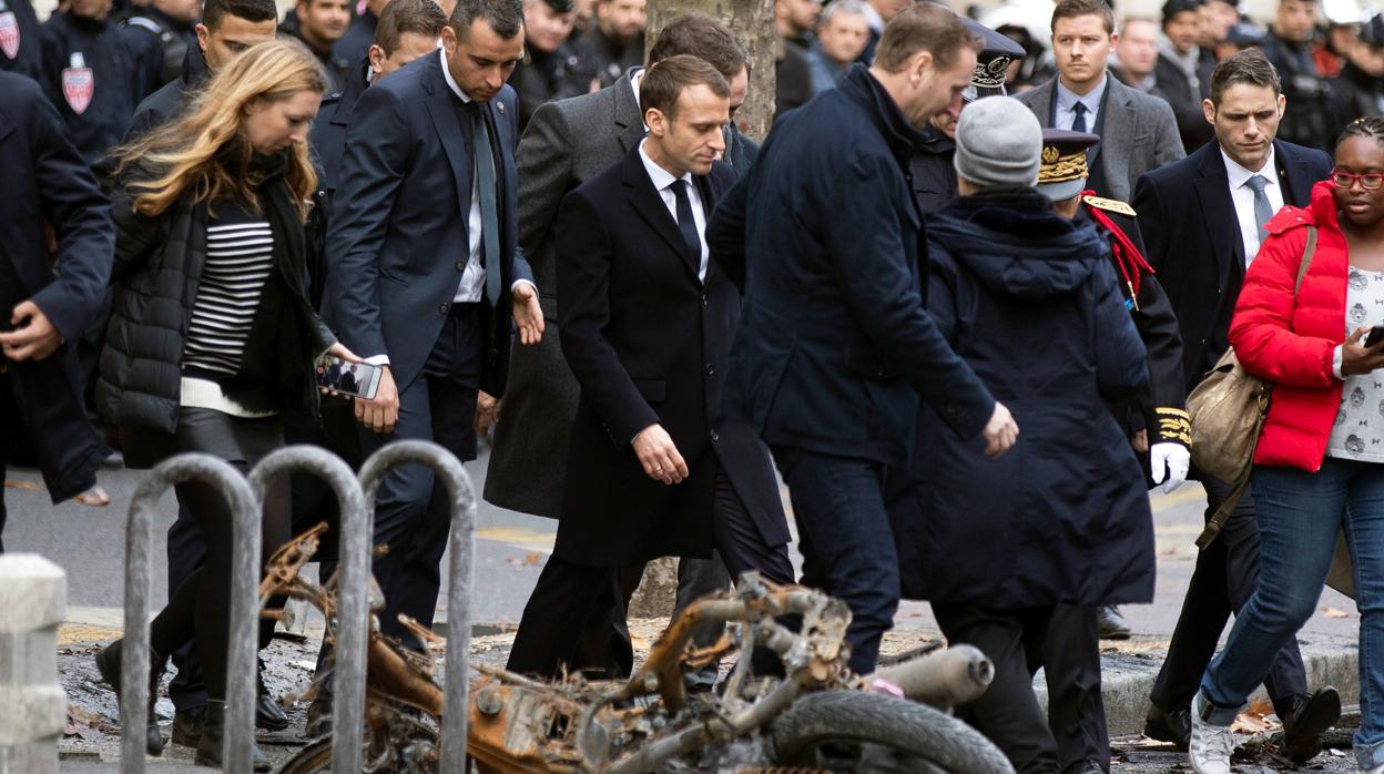 El presidente francés, Emmanuel macron (c), pasa junto a una motocicleta calcinada mientras comprueba personalmente los daños materiales ocasionados en las protestas de los llamados «chalecos amarillos»
