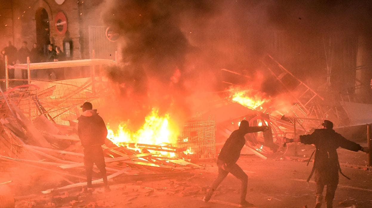 Manifestantes lanzan proyectiles frente a una barricada en llamas