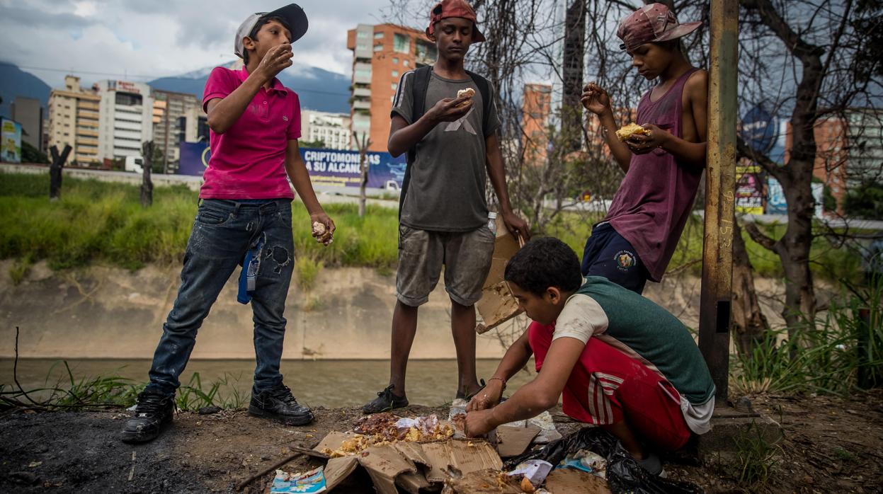 Un grupo de niños busca comida entre bolsas de basura que obtuvieron en una panadería en Caracas