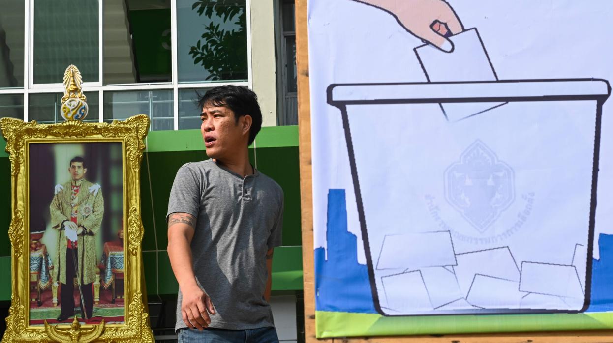 Un hombre pasa frente a un retrato del Rey de Tailandia y un cartel electoral en Bangkok
