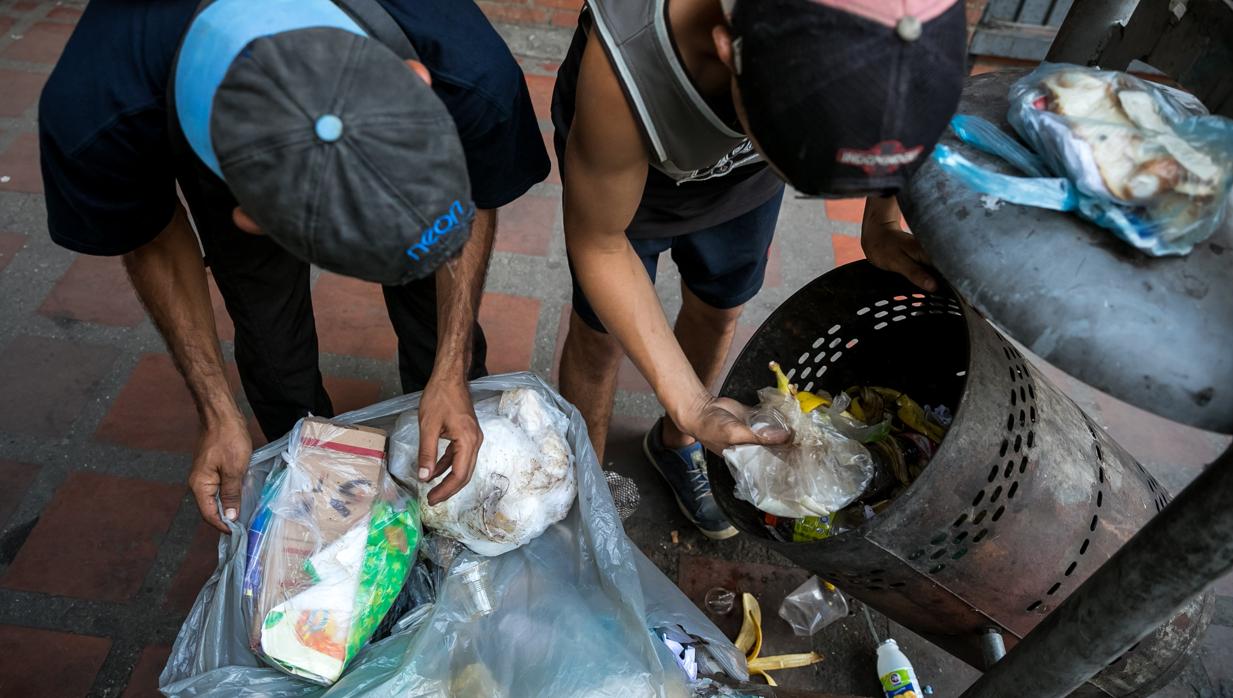 dos hombres mientras hurgan en una basura en busca de comida en una calle de Caracas en 2017
