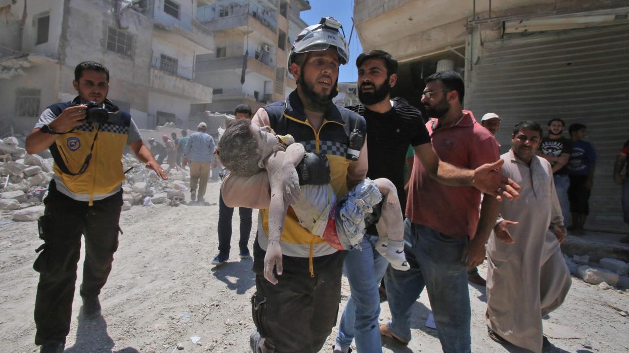 Un miembro de la Defensa Civil Siria (Cascos Blancos) carga con el cuerpo de un niño tras un ataque aéreo en la ciudad de Ariha, en el sur de la provincia de Idlib, Siria