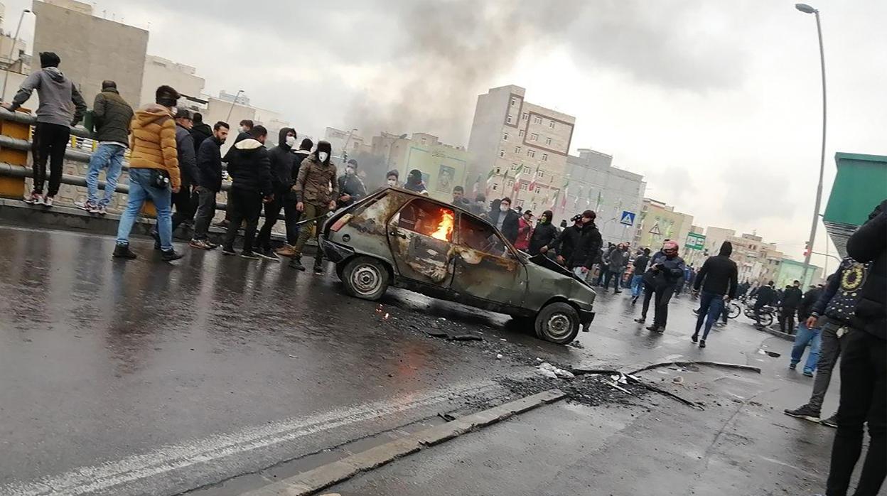 Manifestantes junto a un vehículo en llamas en Teherán