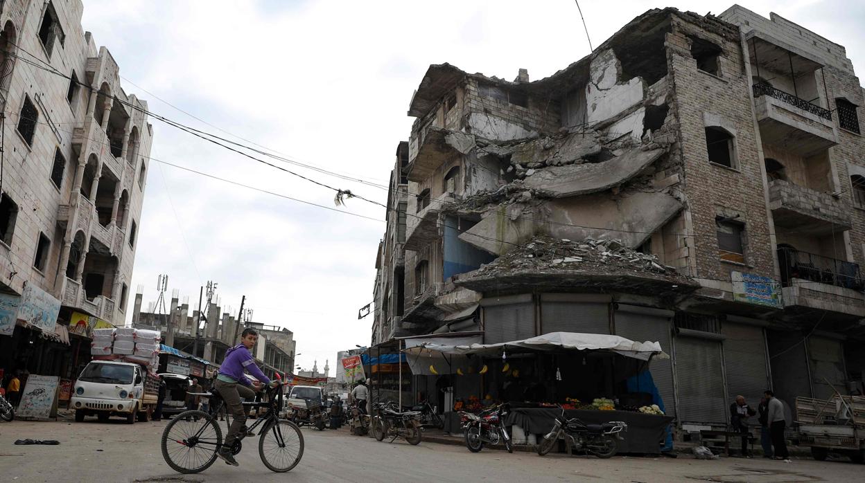 Un joven monta en bicicleta por la ciudad de Idlib, con los edificios destrozados por la guerra