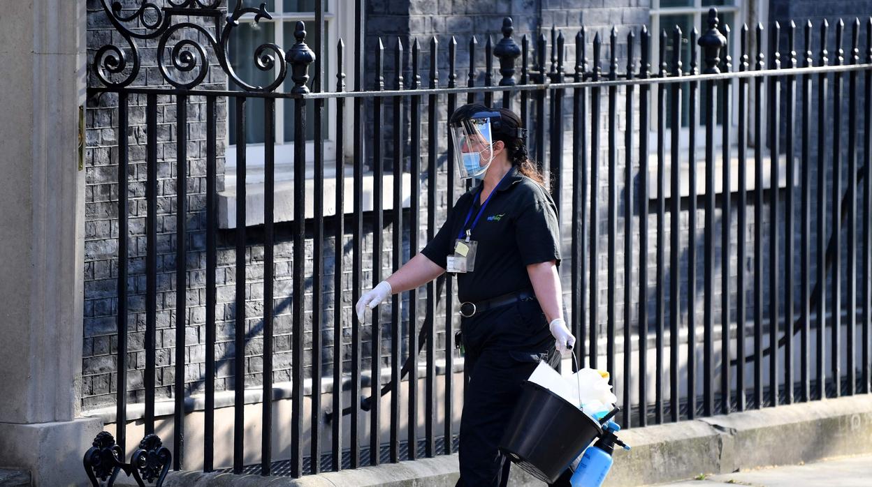 Una mujer con equipamiento de protección y utensilios de limpieza llega a Downing Street