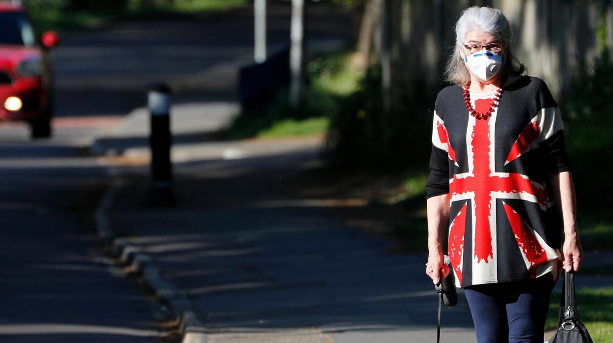 Una mujer pasea con su perro por Londres, protegiéndose con una mascarilla