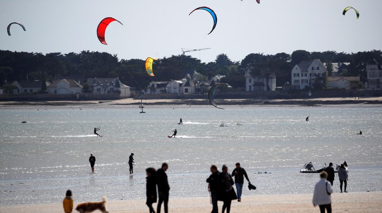 Las personas caminan en la playa mientras los practicantes de kite-surf lo hacen en La Baule