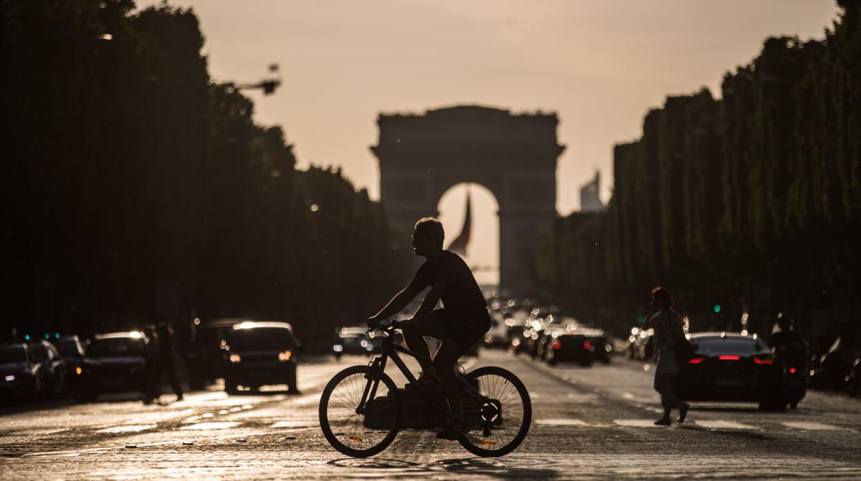 Un ciclista cruza la avenida de los Campos Elíseos de París, con el Arco de Triunfo al fondo