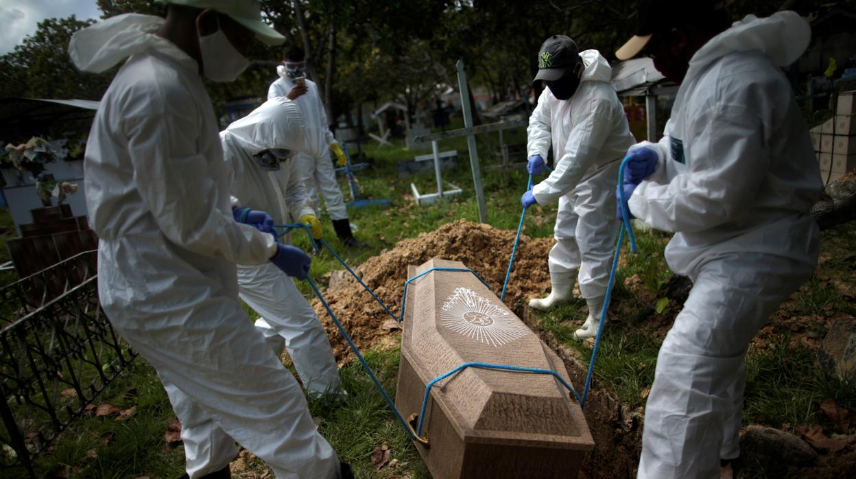 Trabajadores del cementerio Recanto da Paz entierran el ataúd de un hombre que murió por coronavirus