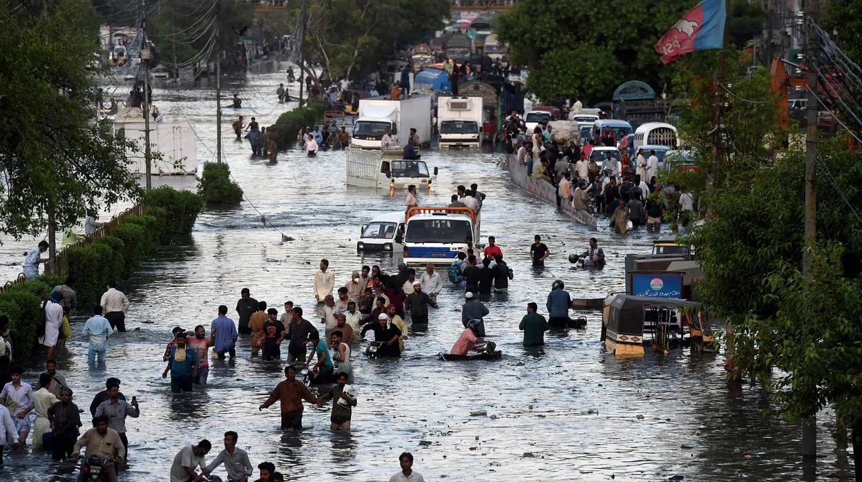 Varios ciudadanos cruzan una calle inundada después de las fuertes lluvias monzónicas caídas en Karachi (Pakistán)