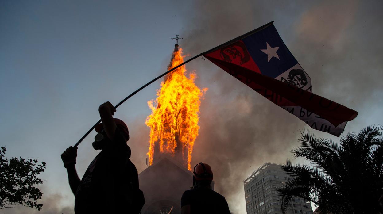 Manifestantes pasan por delante de la Iglesia de la Asunción, mientras esta arde