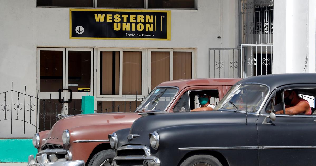 Dos automóviles clásicos pasan frente a una oficina de Western Unión en La Habana