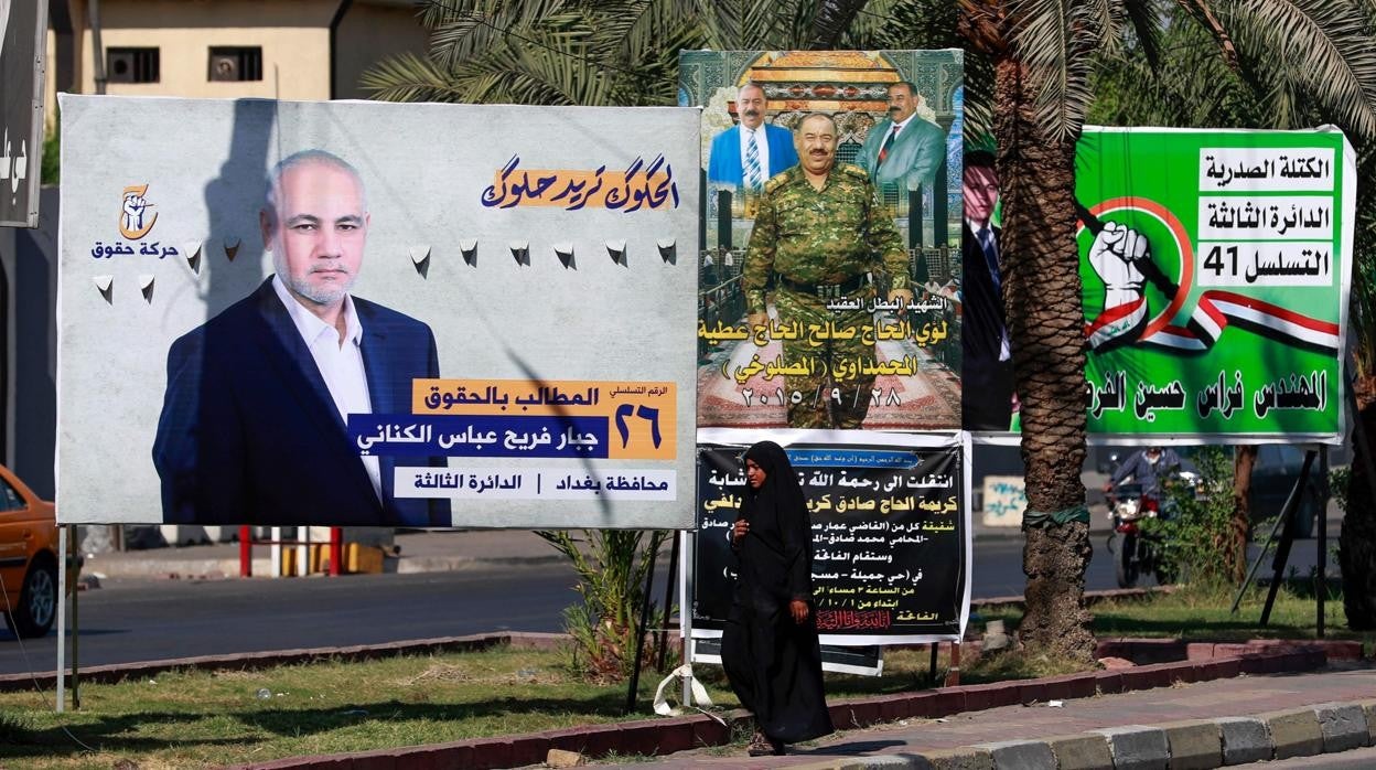 Una mujer iraquí camina por delante de varios carteles electorales en Bagdad