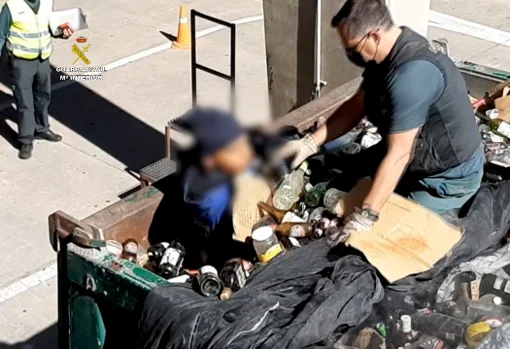 Un agente de la Benemérita saca a un inmigrante de un contenedor de vidrios