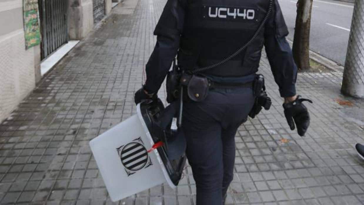 Un policía nacional traslada una urna requisada durante la jornada de ayer