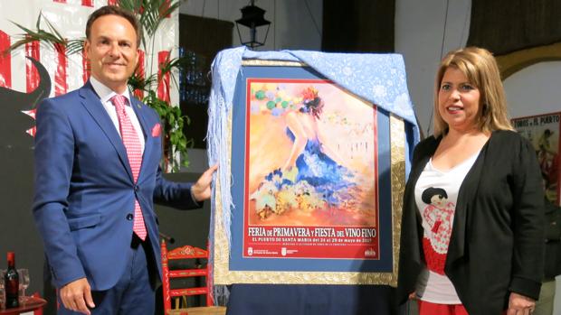 David de la Encina y Mamen Sánchez posan junto al cartel anunciador de la Feria de El Puerto de Santa María.