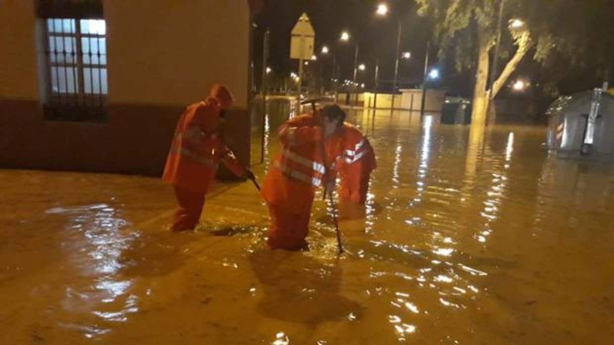 Tres operarios se encargan de desaguar la lluvia en una de las calles de Utrera