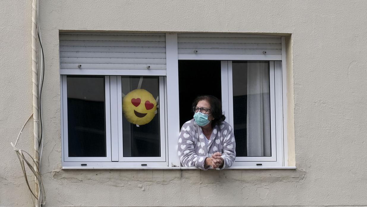 Una vecina de Cádiz asomada en su domicilio con la mascarilla de protección.