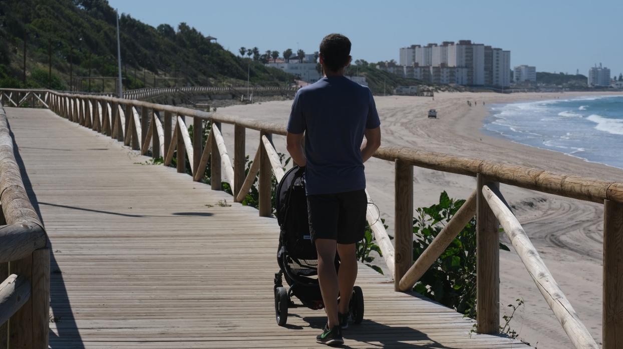 Un padre pasea a su hijo por el paseo marítimo de la playa de Las Redes, en El Puerto.