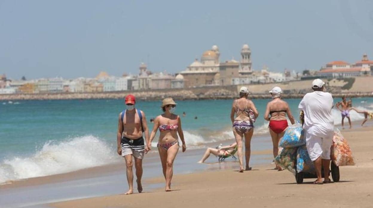 Bañistas en la playa de Cádiz cumplen la obligación de llevar mascarilla para pasear por la arena.