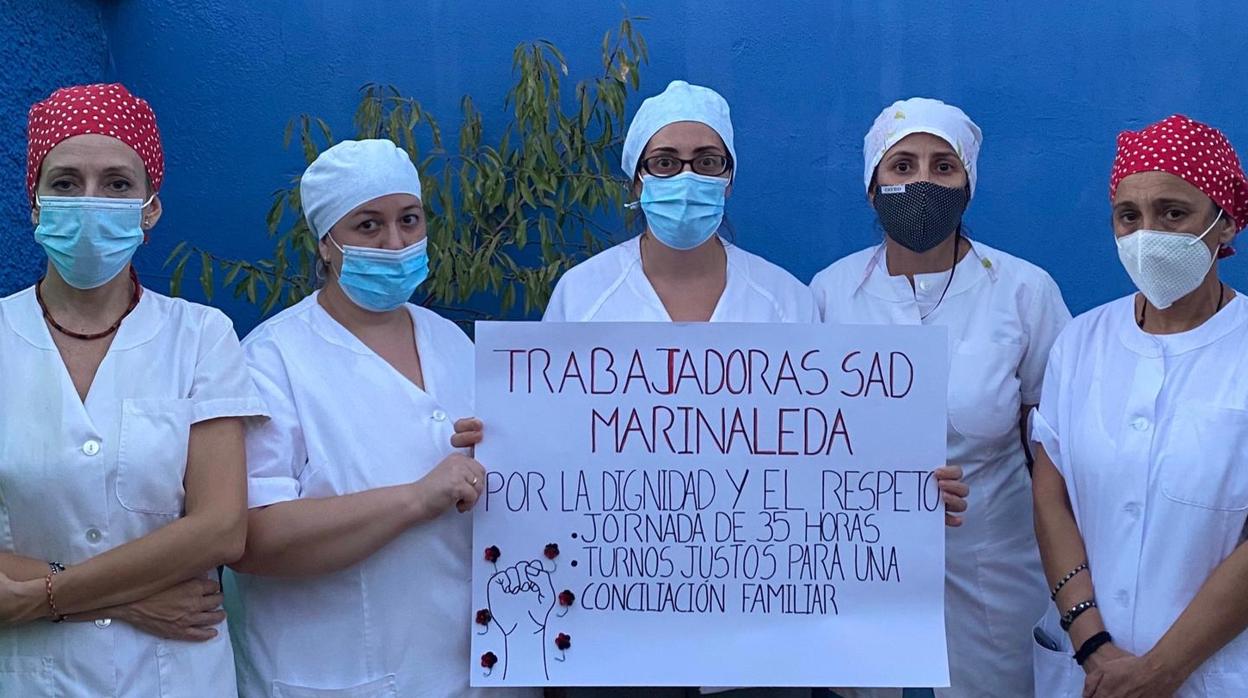 Cinco trabajadoras de ayuda a domicilio de Marinaleda con una pancarta reivindicativa por sus derechos laborales