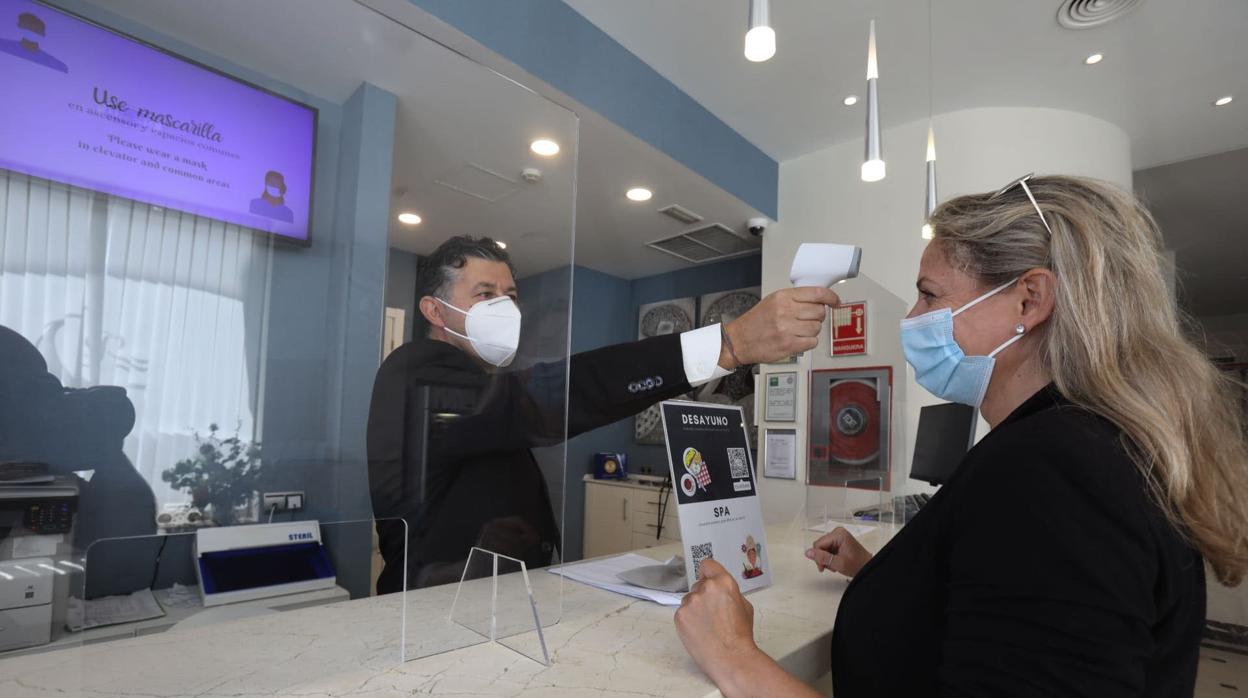 Pruebas de toma de temperatura a los clientes en la recepción de un hotel de Cádiz.