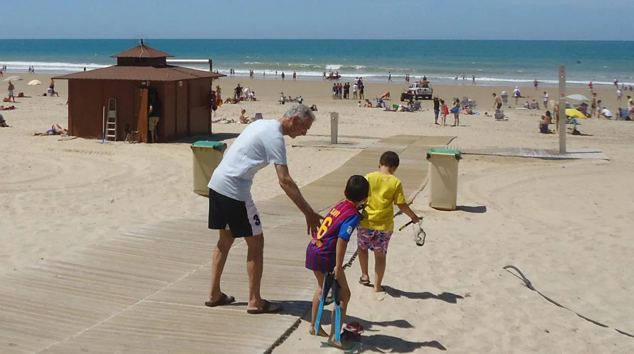 Un hombre accede a la playa junto a dos niños por una de las pasarelas.