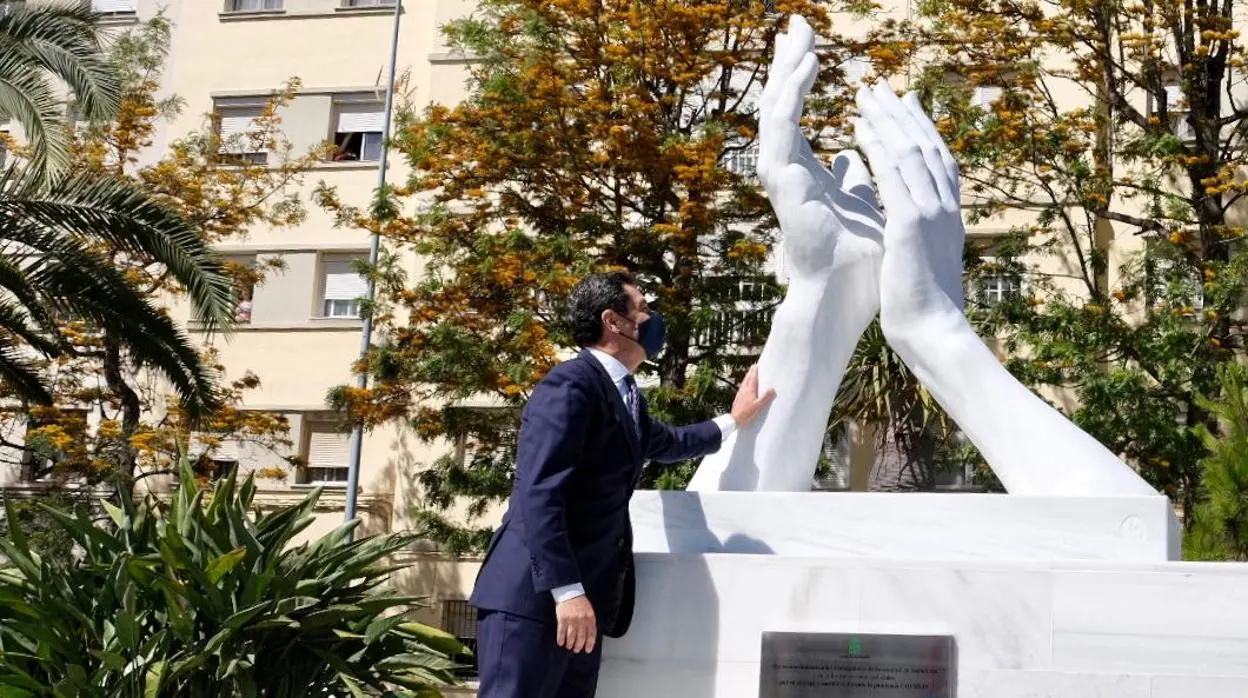 El presidente de la Junta de Andalucía, Juanma Moreno, junto a la escultura de homenaje a los sanitarios.
