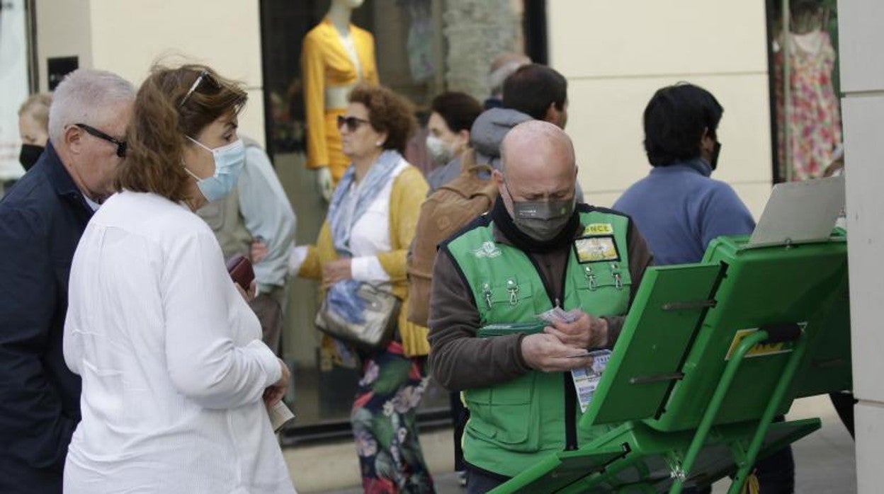 Un vendedor de cupones de la Once en una calle de Sevilla atiende a unos clientes