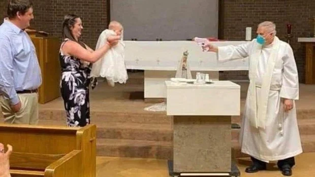 Un sacerdote utiliza una pistola de agua para bautizar a un bebé respetando la distancia de seguridad