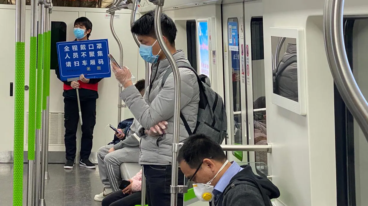 Hombre-anuncio con un cartel en el metro de Wuhan recordando la obligación de llevar mascarilla y evitar las aglomeraciones