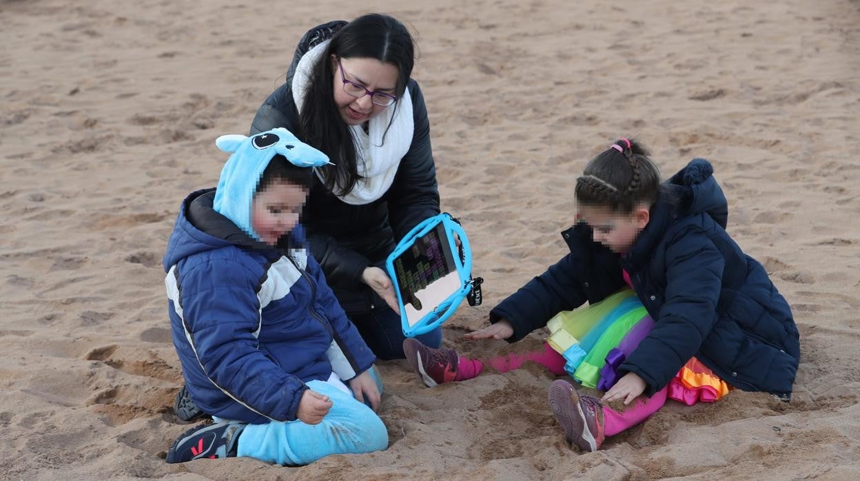 La madre de Yago, Marta Lázaro, intenta comunicarse a través de un ordenador con su hijo, que padece síndrome de Angelman, en la playa del Arbeyal de Gijón donde sus hijos, con disfraces infantiles de carnaval, juegan con la arena de la playa