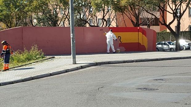 Un operario tapa con pintura color terracota la bandera española en Bueno Monreal