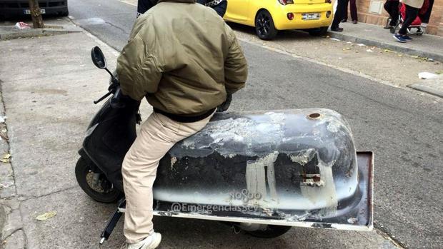 Un individuo transporta una bañera en su ciclomotor Piaggio Zip.