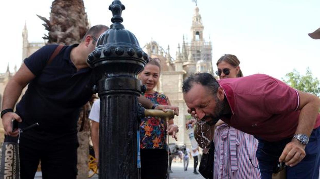 Unos turistas se refrescan en una fuente del centro de Sevilla
