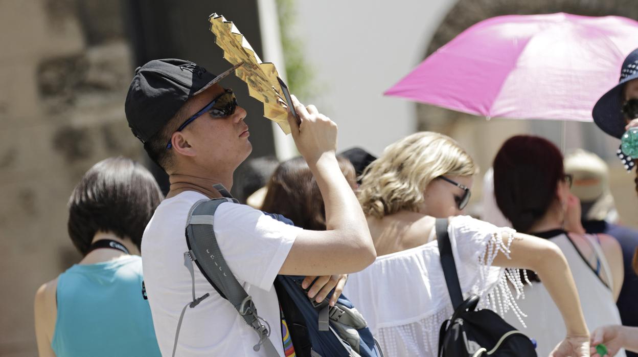 Un joven se protege del Sol con un abanico mientras pasea por Sevilla